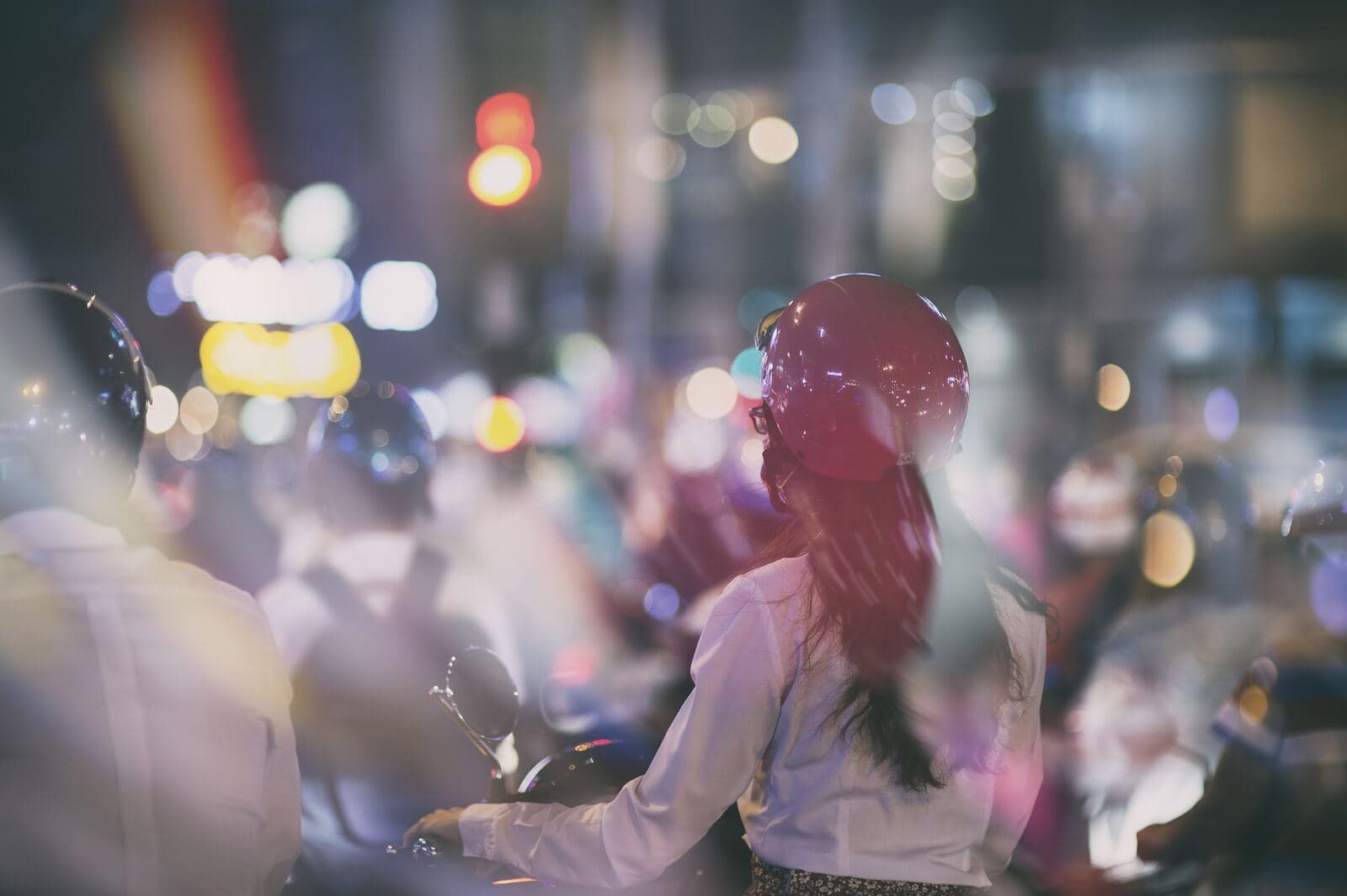 Người đội mũ bảo hiểm đỏ chờ đèn giữa dòng xe buổi tối, nhìn từ phía sau